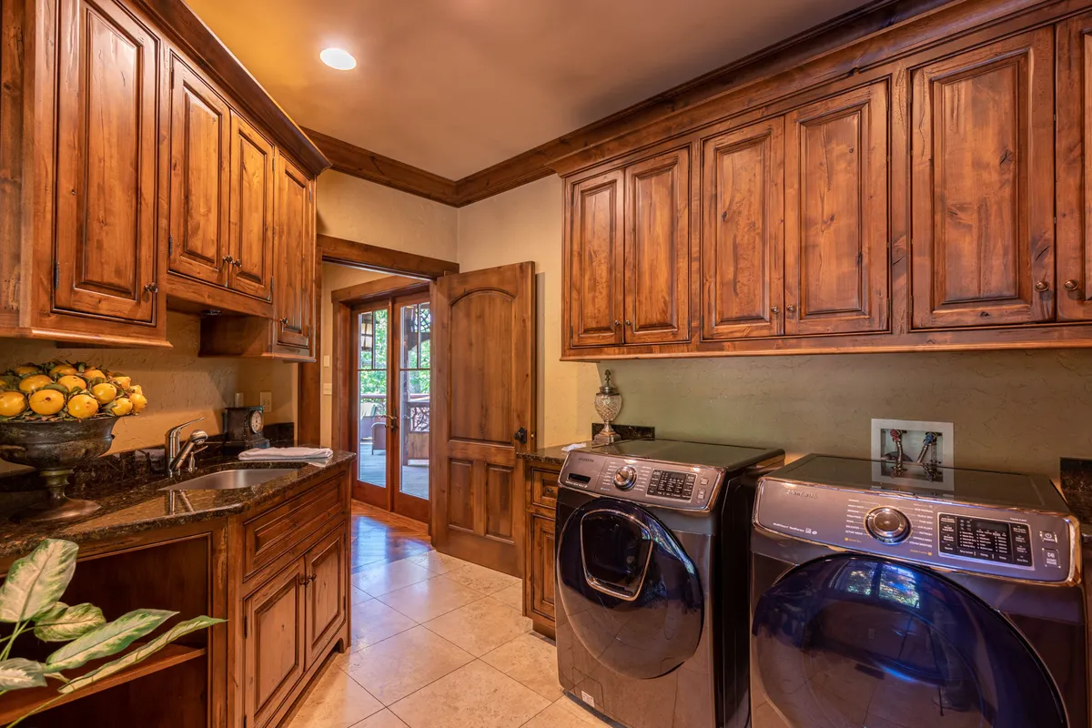 A functional yet cozy laundry room with wooden cabinets, a washer and dryer, a sink, and a doorway leading outside. The space feels organized and accessible, making everyday chores convenient for guests.