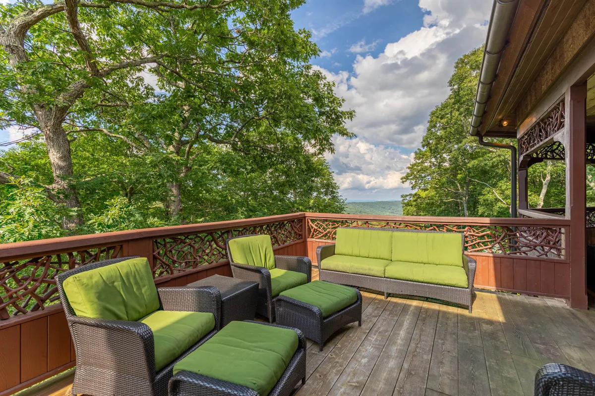 A serene deck overlooks water and trees, with comfortable green-cushioned furniture and a beautifully crafted wooden railing. The space is ideal for quiet reflection or casual gatherings, immersed in the surrounding beauty.
