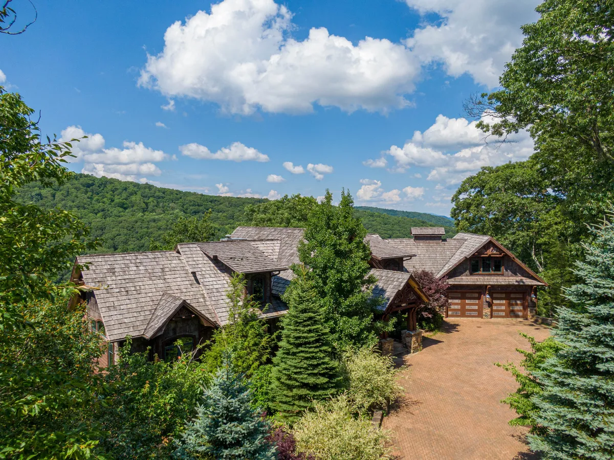 This image showcases the main house nestled among tall trees, with a spacious driveway leading up to it. The setting suggests a peaceful, nature-immersed retreat, ideal for both quiet mornings and group gatherings. The surrounding woods and the home’s inviting exterior give a strong sense of seasonal change and outdoor exploration.