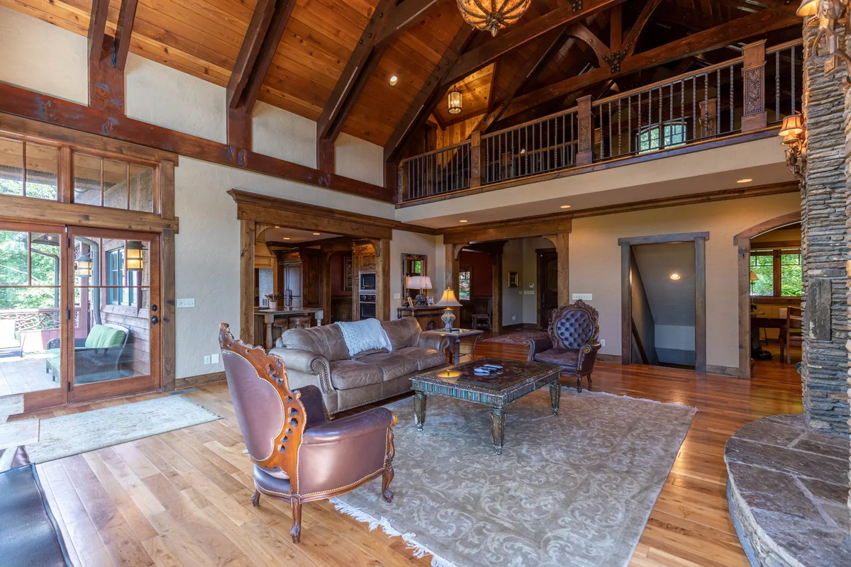 A spacious living area is shown with a high wooden ceiling, elegant fireplace, and luxurious leather seating. Sunlight streams through the large windows, illuminating the signature Timberlake design elements throughout the space.