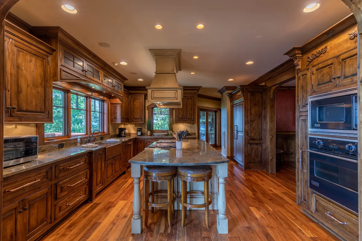 A close-up view of a kitchen with a granite countertop, wooden cabinetry, a kitchen island, and high-end stainless steel appliances. The warm, cozy atmosphere invites both everyday meal prep and entertaining family or guests.