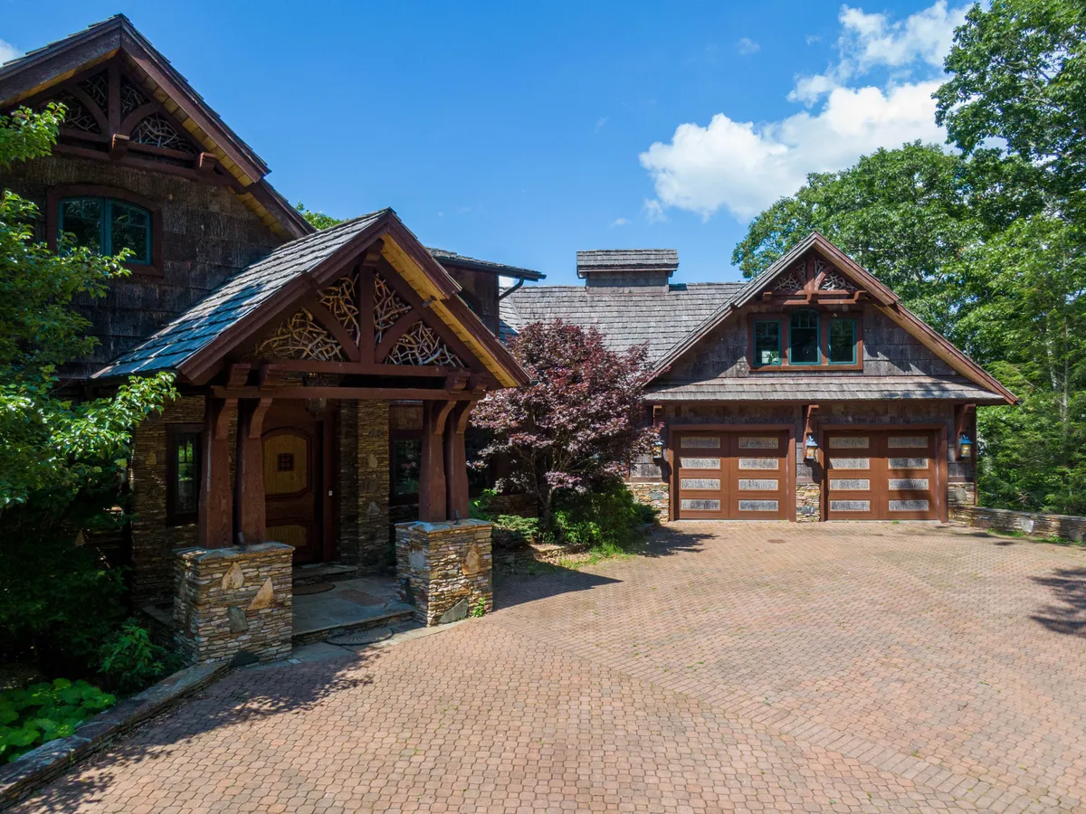 This image captures the home's ornate entrance with impressive stonework and wooden accents, framed by manicured landscaping. The scene is awash in warm light, hinting at sunset, and the atmosphere is one of calm invitation, evoking the feeling of arriving at a finely crafted, artistic retreat.