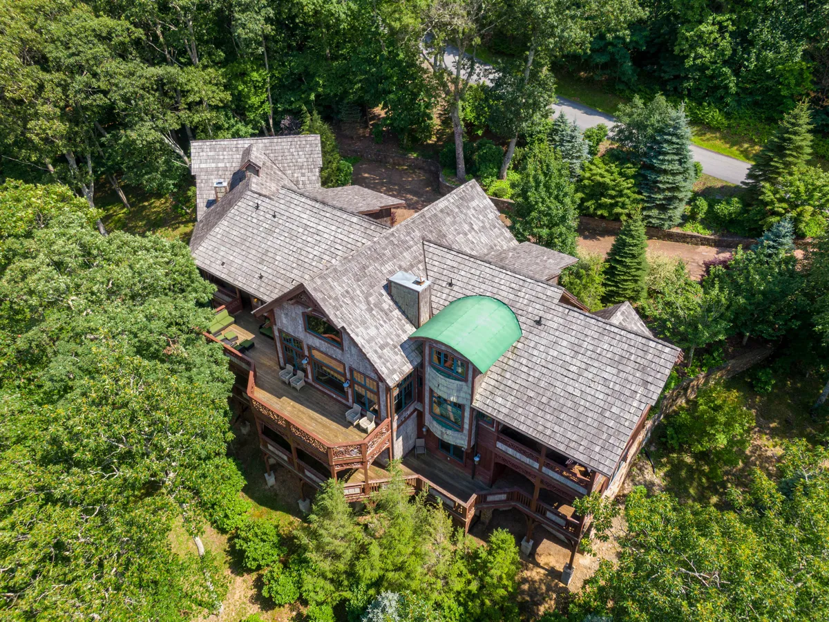The photo highlights the home's unique architecture with a green roof accent and spacious deck, surrounded by lush greenery. The tranquil outdoor setting invites relaxation and connection with nature, seamlessly blending the built environment with the mountain landscape.