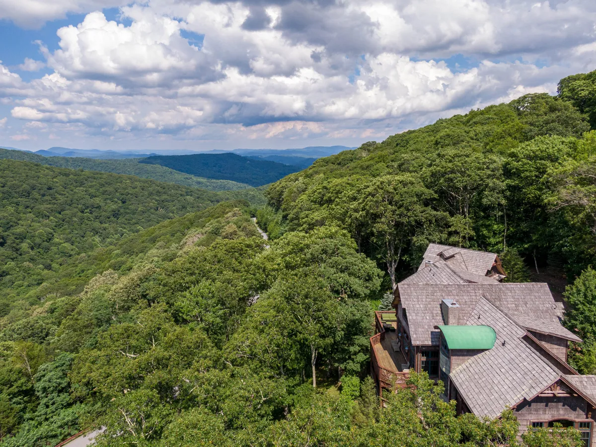 A panoramic exterior shot showcasing the property’s wooden architecture set against a stunning mountainous landscape and an expansive sky. The image highlights the sense of seclusion and adventure, with hints of hiking and wildlife observation opportunities in the surrounding terrain.