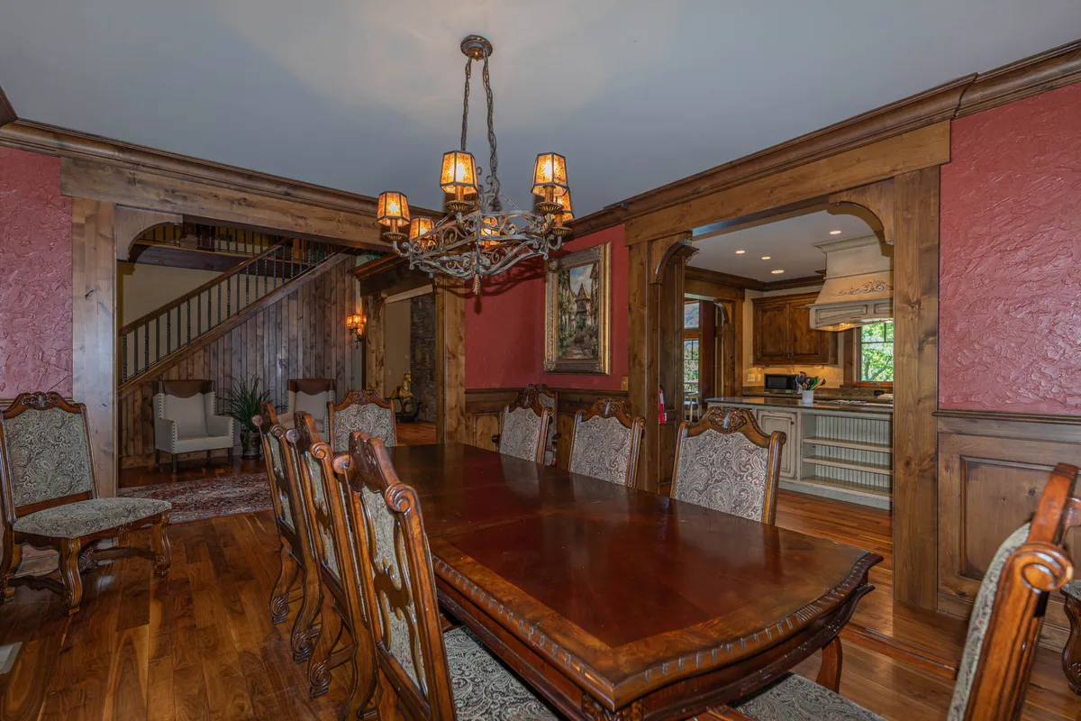 A spacious dining area with a large wooden table that seats ten, ornate chairs, and a chandelier overhead. The red walls and elegant decor create an inviting space for festive feasts and large gatherings.