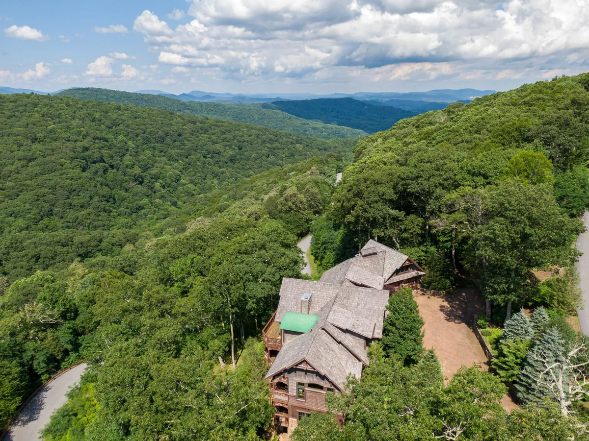 This exterior shot captures the house tucked among mature trees with a breathtaking mountainous landscape and a winding road leading into the distance. The setting is tranquil and immersed in nature, evoking the sense of adventure and exploration available just outside the home.