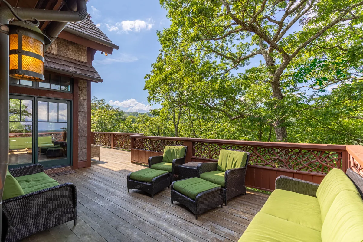 An exterior view featuring a comfortable seating area overlooking a tranquil lake, surrounded by lush greenery. The space is designed for relaxing outdoors, taking in the scenery, and socializing with friends or family. The serene lake and vibrant plant life suggest a perfect backdrop for spring, summer, and autumn activities.
