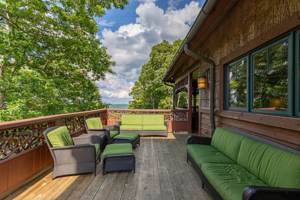 A tranquil outdoor seating area on a wooden deck, framed by intricate railing and set against a lush green landscape. The inviting furniture suggests a space for stargazing, sipping morning coffee, or enjoying celebrations at sunset.