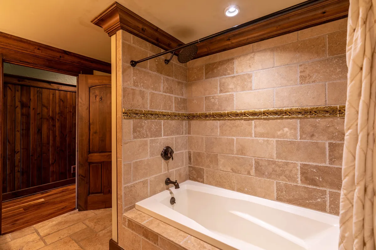 A spa-like bathroom with a bathtub, decorative tile, and wooden accents, inviting relaxation and self-care. The tranquil mood and luxurious finishes offer a glimpse into the retreat’s four full bathrooms, designed for privacy and comfort.