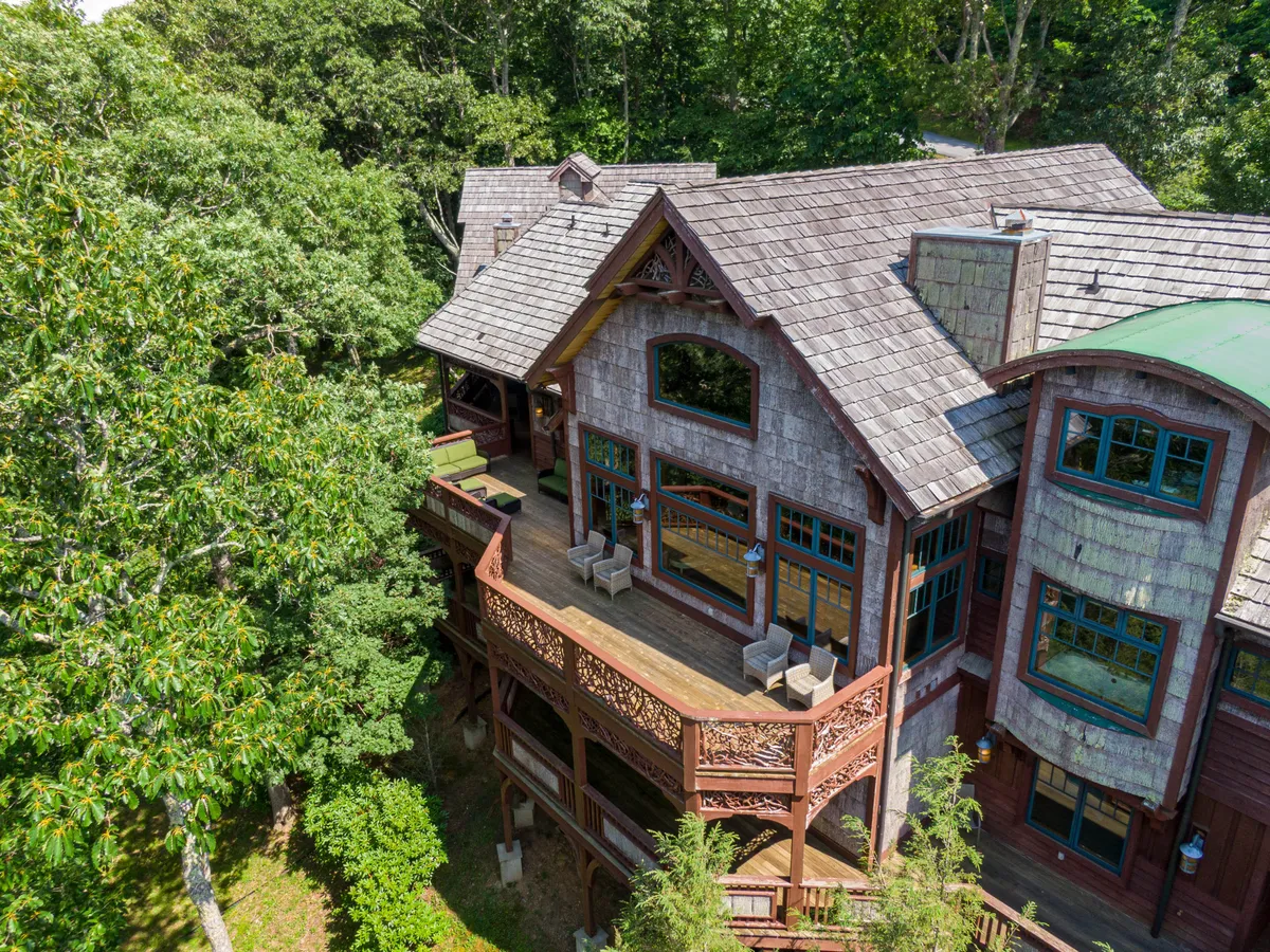 A wide view of the home's expansive deck, featuring intricate woodwork, large windows, and an inviting outdoor gathering area. The deck overlooks lush greenery and is ideal for relaxing after a day on the trails or letting your pup rest nearby as you unwind.